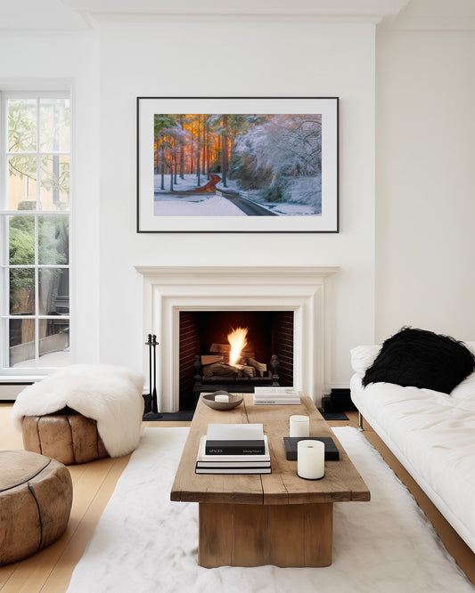 Modern living room with a fireplace, wooden coffee table, and framed artwork of a winding road through a snowy forest with trees illuminated with a sunrise in south arkansas.