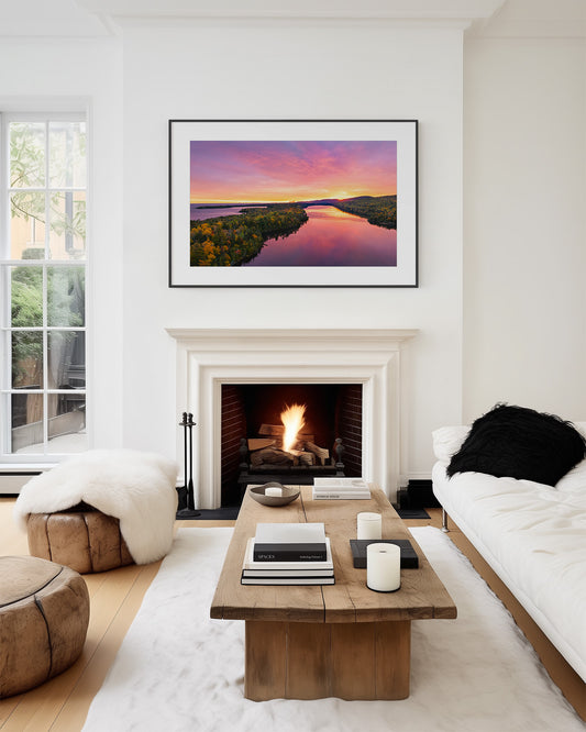 A framed sunrise landscape art print of an Aerial view of Lake Fanny Houe is displayed on a white wall above a fireplace in a modern, stylishly decorated living room.