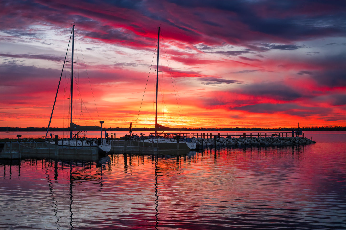 Northport Marina on Grand Traverse Bay with sailboats at sunrise under a vibrant red, orange and blue sky.