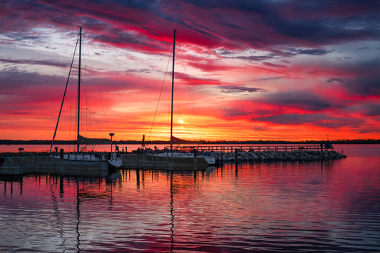 Northport Marina on Grand Traverse Bay with sailboats at sunrise under a vibrant red, orange and blue sky.