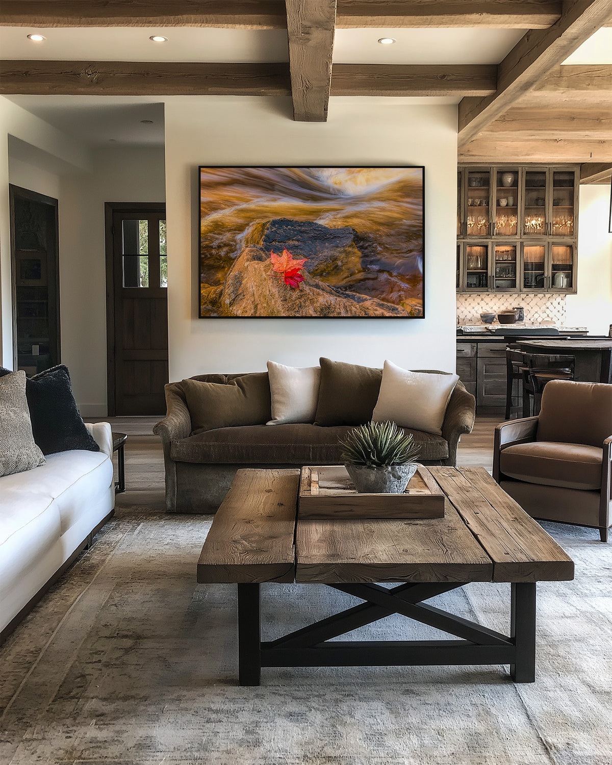 A framed landscape art print featuring a golden sunset over rocky terrain with a red maple leaf, displayed on a white wall in a modern rustic living room setting.