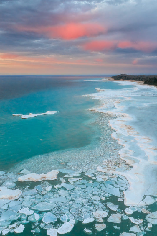 Aerial fine art photograph of Lake Michigan winter sunset with soft pink and teal sky over icy shoreline textures