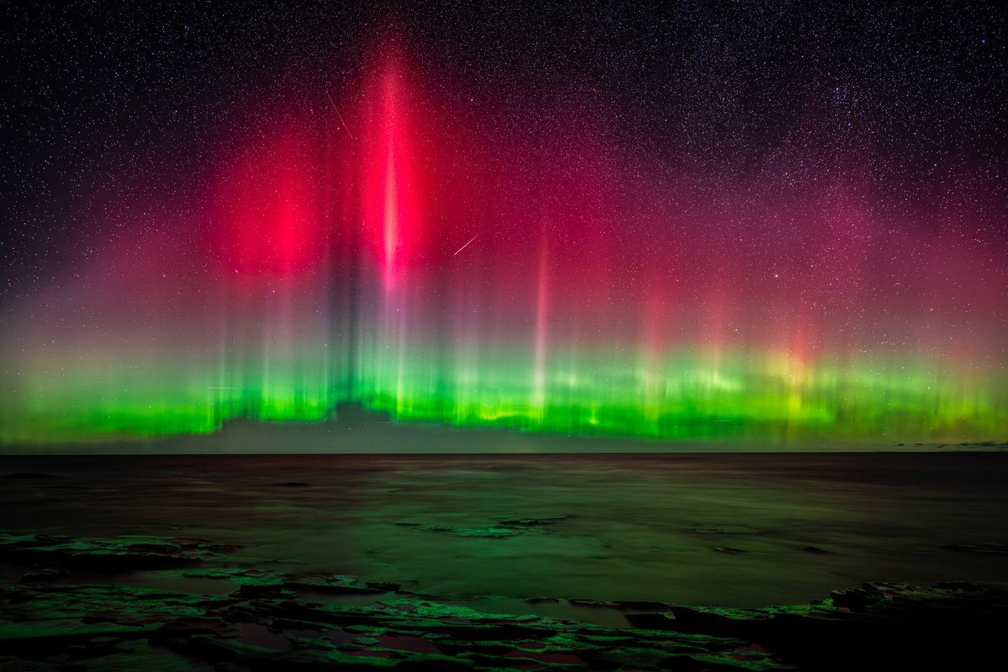 Brilliant emerald green and bright pink Aurora borealis with stars and a meteor against a dark sky