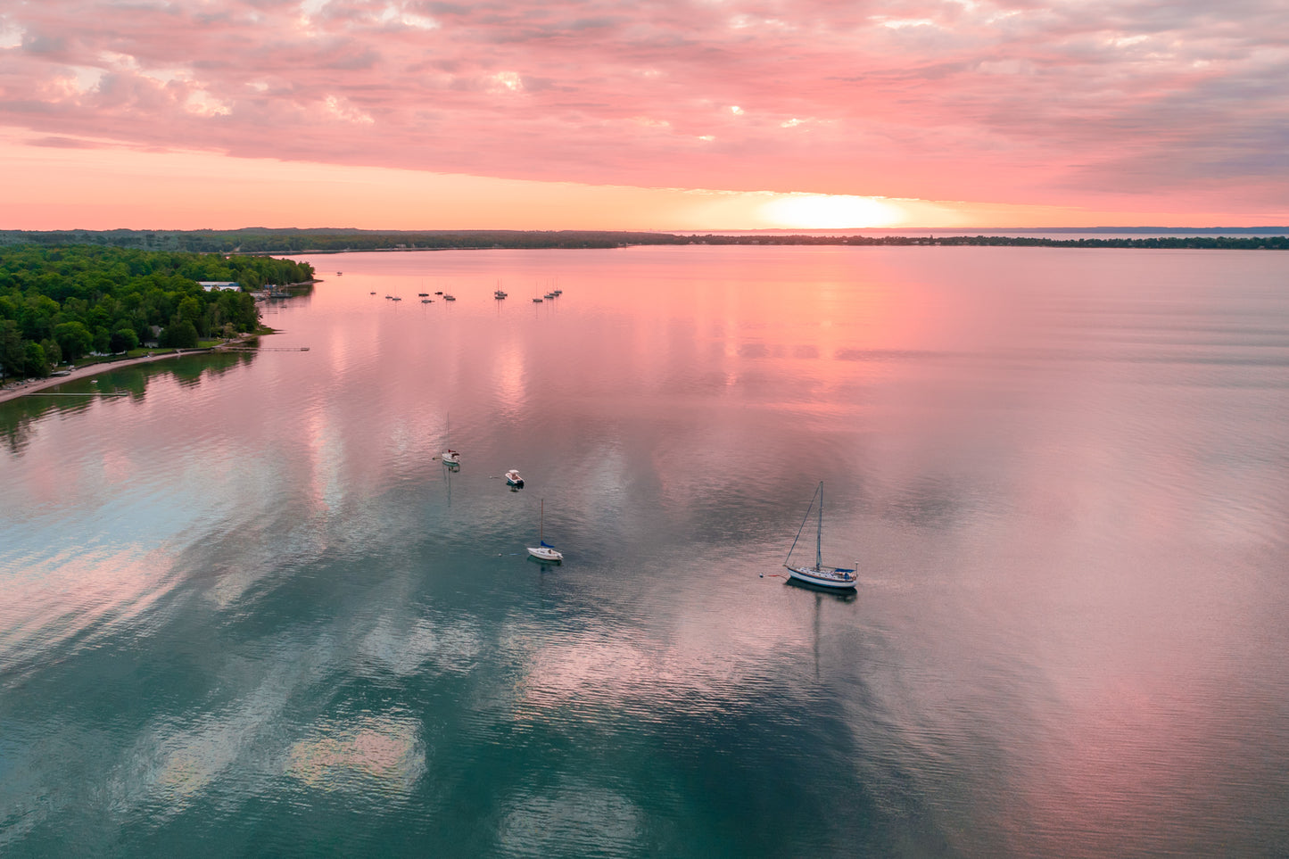 Aerial view of Grand Traverse Bay with boats at sunset, reflecting pink and orange colors on the water.