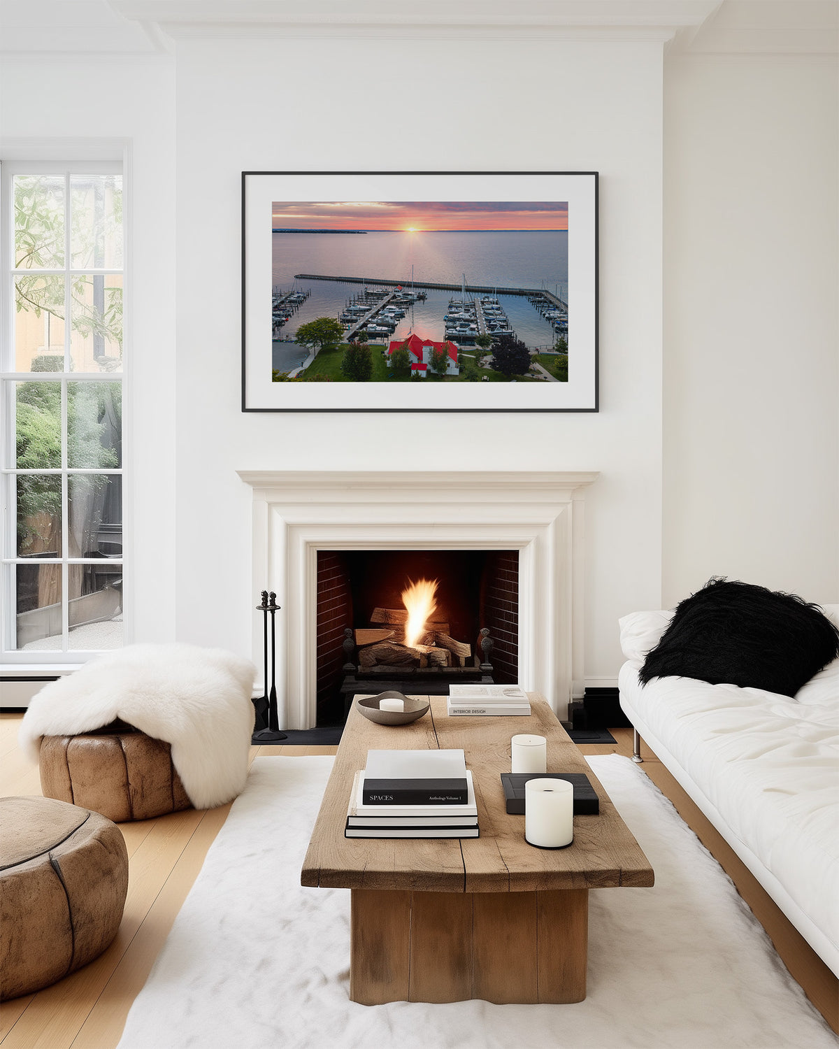 A framed art print of a sunset marina scene hangs on a white wall above a fireplace in a modern, bright living room with a wooden coffee table, white sofa, and wood floor. Northport, Michigan.  Grand Traverse Bay.