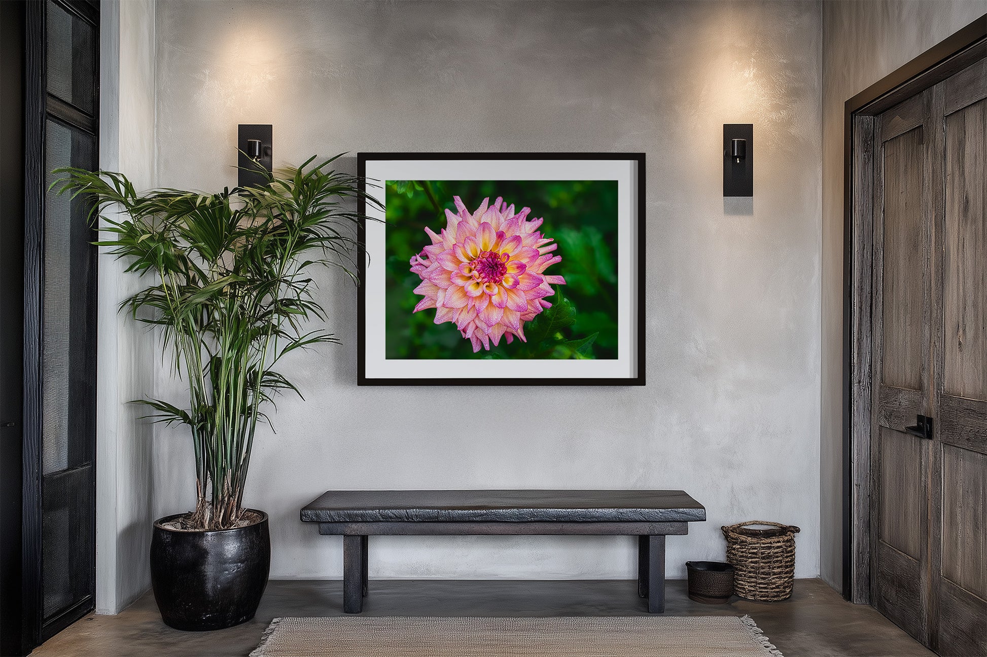 Framed picture of a pink dahlia flower with green background on a wall above a bench in a room with a plant and door.