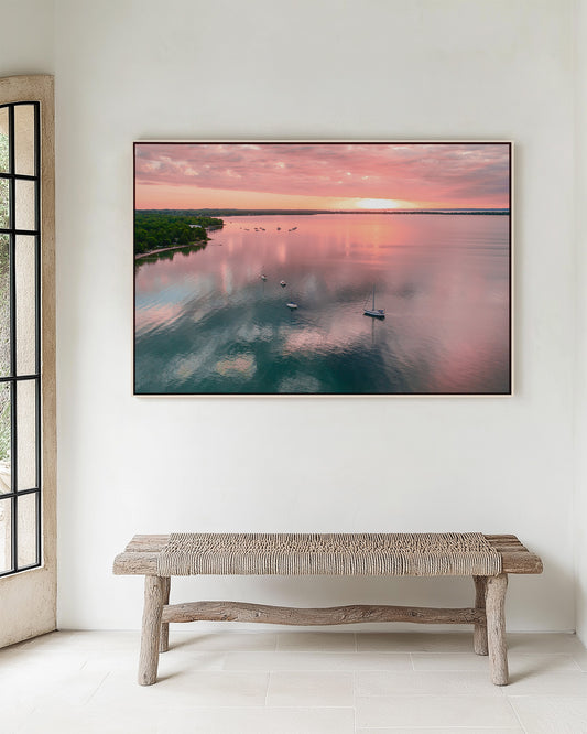 Framed artwork of aerial view of Grand Traverse Bay sunrise in Northport Michigan hanging on a wall above a wooden bench.