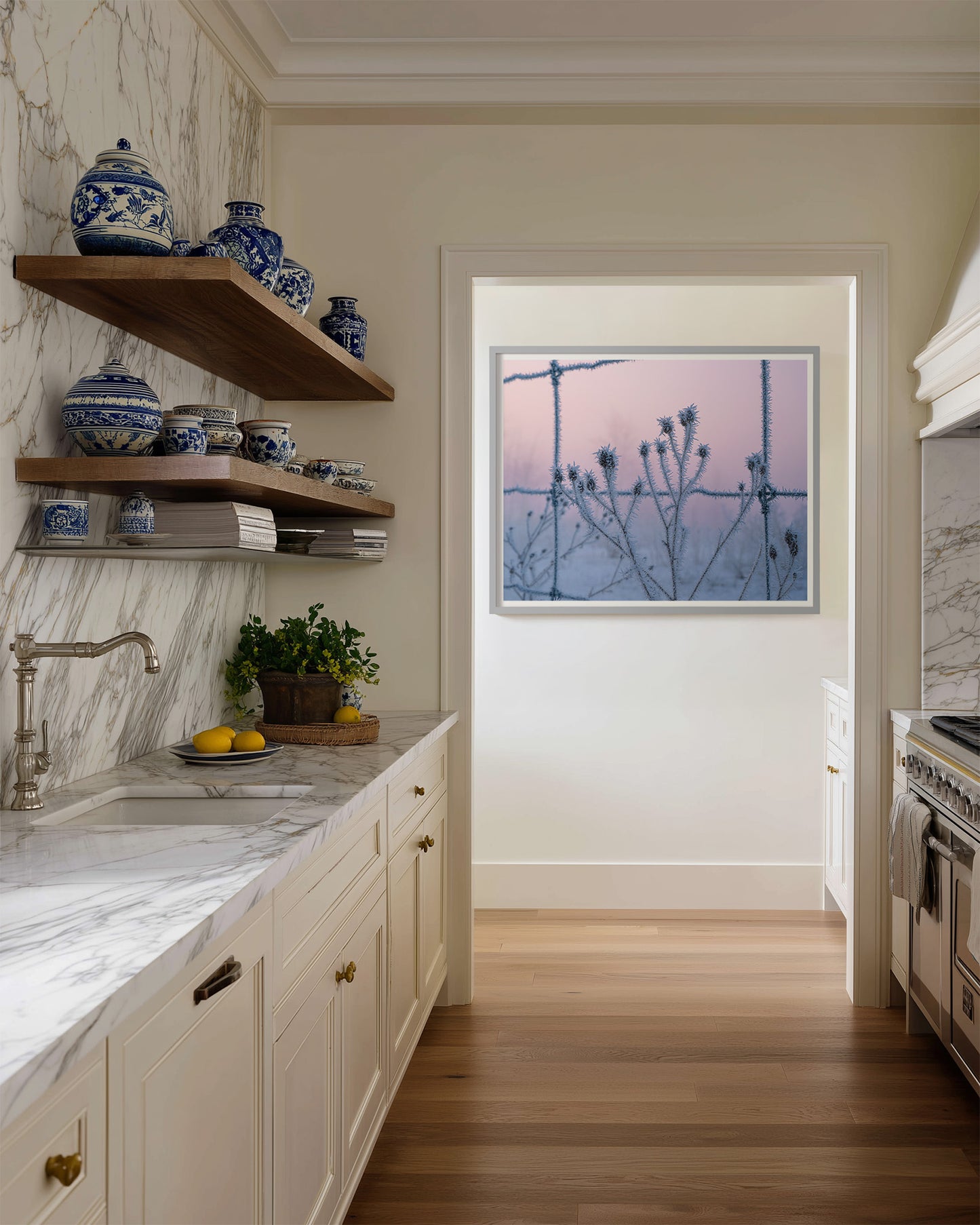 Modern kitchen with marble countertops, wooden shelves, and a painting fo hoar frost covered branches through a barbed wire fence with a pastel sunrise sky.