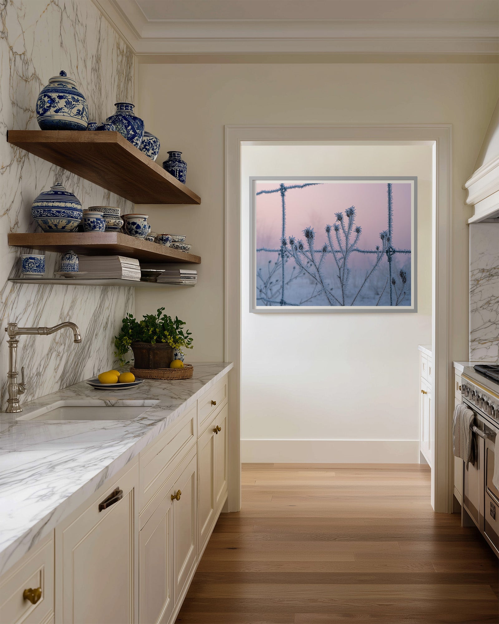 Modern kitchen with marble countertops, wooden shelves, and a painting fo hoar frost covered branches through a barbed wire fence with a pastel sunrise sky.