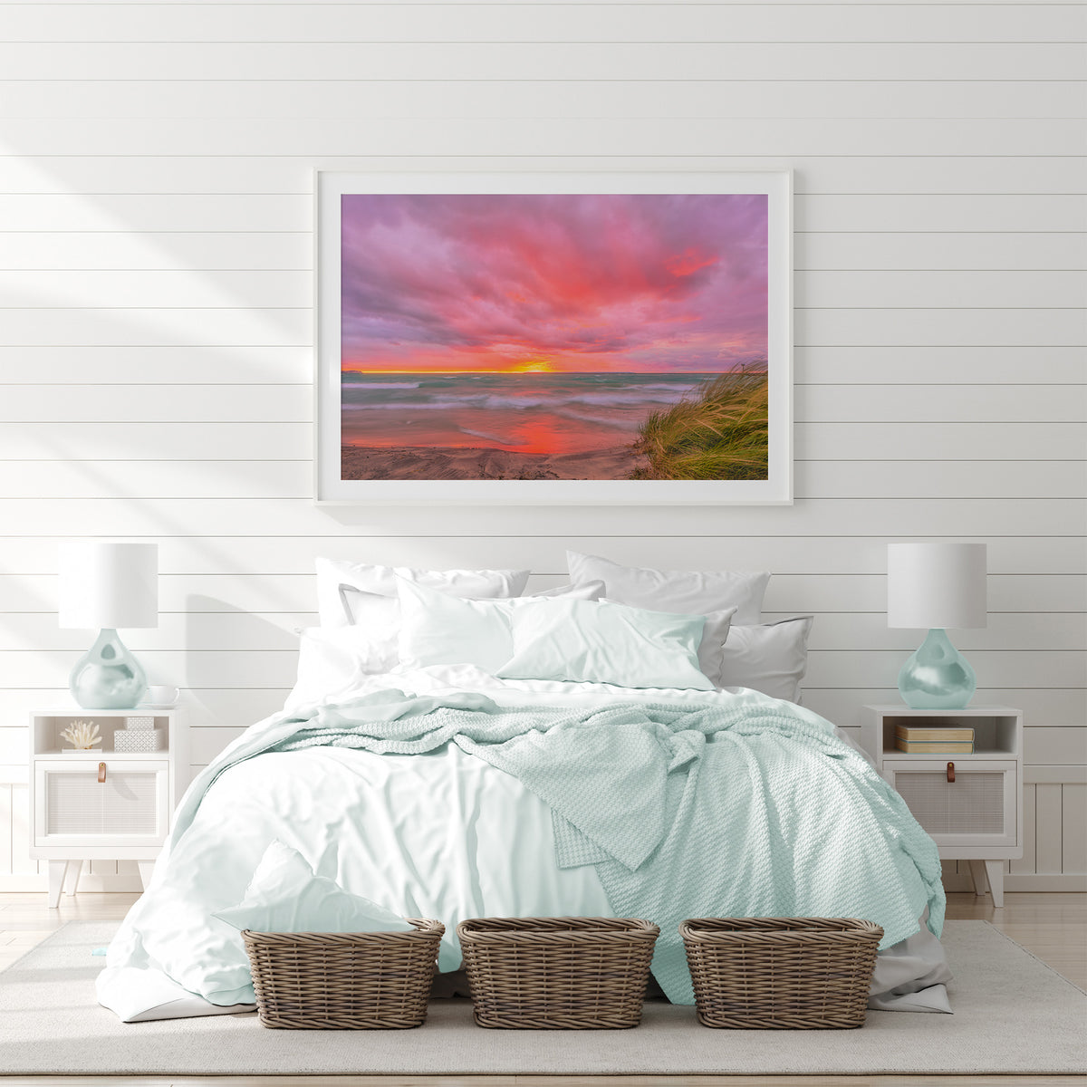 Framed scenic landscape of  Lake Michigan, Van's beach at sunset, featuring dramatic pink and orange clouds, turquoise water, wet sand reflecting the sky, and grass in the lower right foreground.