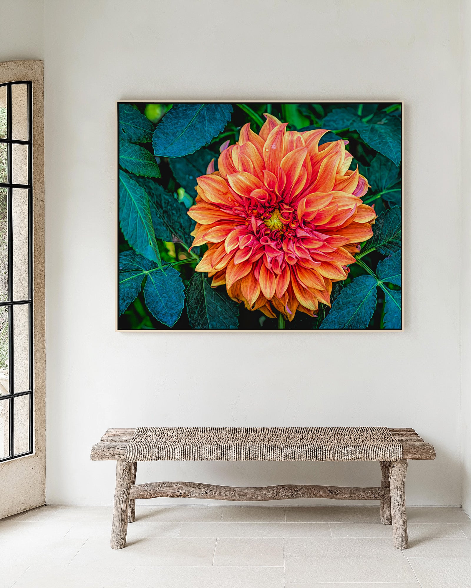 Framed artwork of a vibrant orange dahlia flower with green leaves on a white wall above a wooden bench.